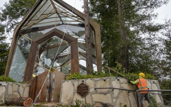 Chapel seen amidst trees, maintenance worker seen in bottom right corner. 