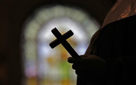 Image of a crucifix silhouetted against a stained glass window. 