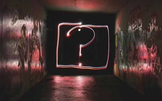 A question mark in light down a dark, graffitied hallway (Unsplash/Emily Morter)