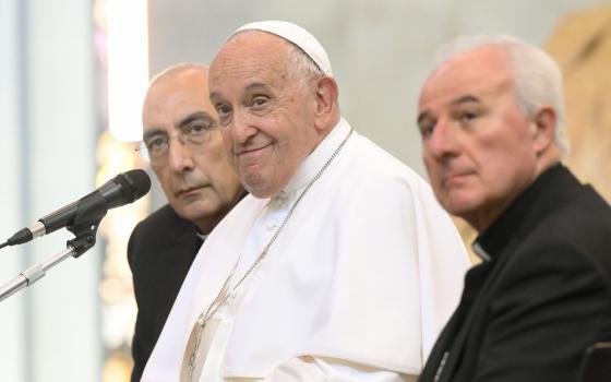Pope Francis, seated, smiles as he listens. 