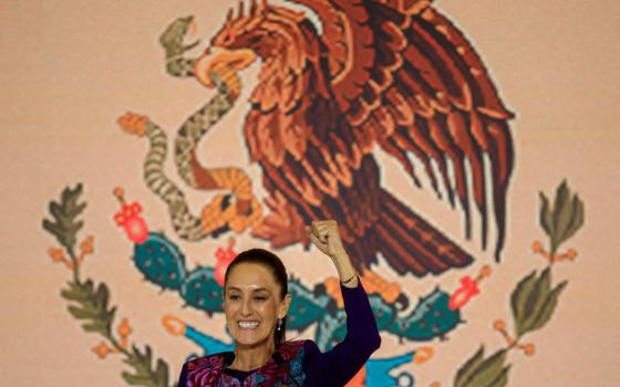 Scheinbaum smiles and raises fist in victory in front of banner bearing Mexico's eagle emblem.