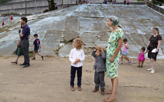 Woman stands with two children, as others walk in background