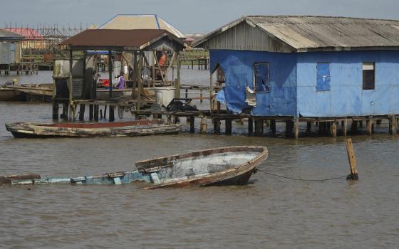 In background are houses on stilts, sitting just barely above the water line, and foregrounded is a partially submerged boat tied to dock. 