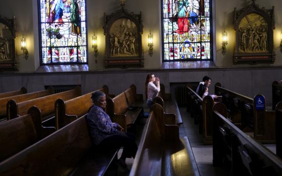 Stained glass windows, stations of the cross, and people kneeling. 