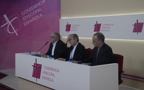 Officials sit at panel desk during press conference. 