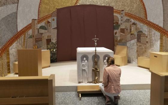 Woman kneels at small altar, behind altar are Rupnik's mosaics. 