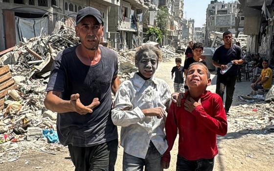 A man and two children walk through rubble; one child's face is completely white with dust, and the other sobs. 
