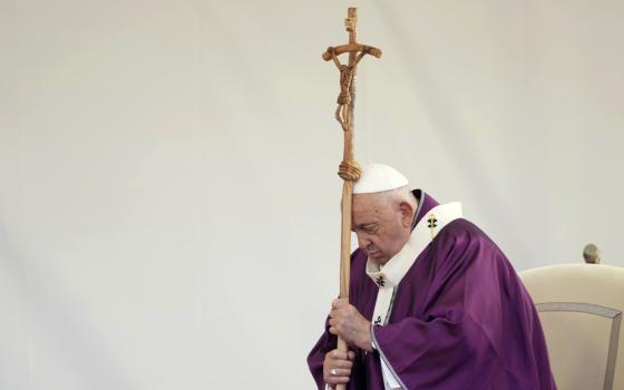 Pope, vested in penitential purple, stands, and leans head on processional cruxifix.