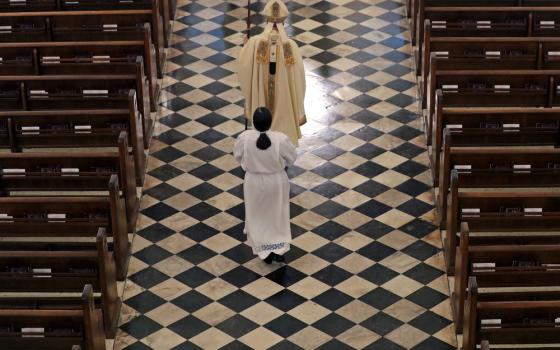 Vested archbishop processes through aisle followed by acolyte.