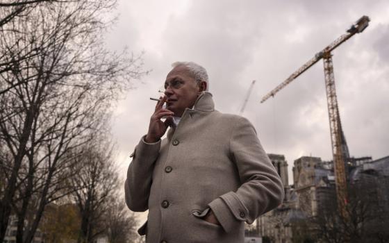 Villeneuve wears coat, smoking, in background is massive crain.