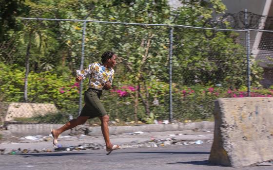 A woman runs to take cover from gunfire during clashes between police and gangs in the Delmas neighborhood of Port-au-Prince, Haiti, Dec. 2, 2024. (AP/Odelyn Joseph)