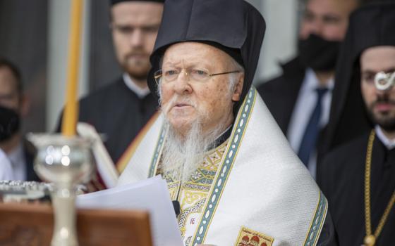 Patriarch in vestments standing at lectern reading from written speech.