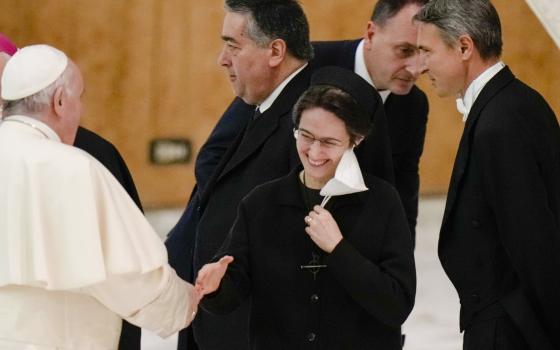 Sr. Petrini smiles at the Pope who is shown from behind shaking her hand.