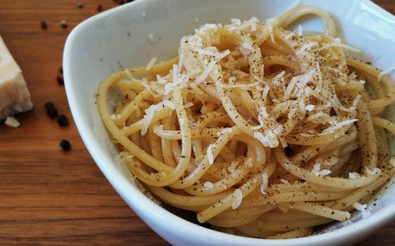 Cacio e pepe in a white bowl with ingredients on a wooden table (Wikimedia Commons/Popo le Chien)