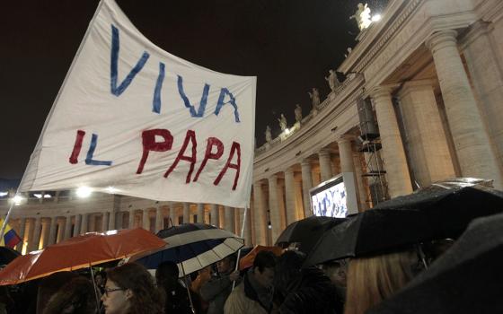 Pilgrims wave a banner saying "Viva il papa" ("Long live the pope") as white smoke rises from the chimney above the Sistine Chapel, indicating a new pope has been elected at the Vatican, in this photo from March 13, 2013. The conclave to elect a new pope met over two days before making a decision. (CNS/Reuters/Giampiero Sposito)