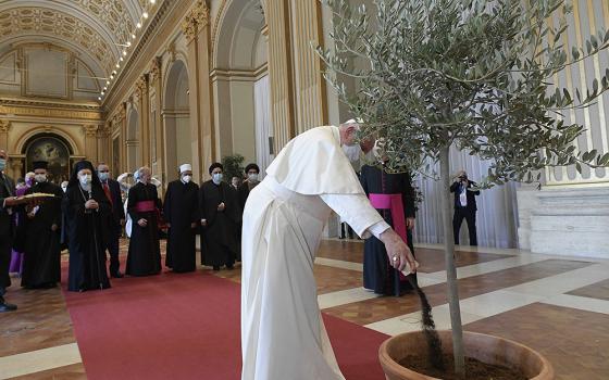Pope Francis pours dirt into a potted olive tree during the meeting, “Faith and Science: Towards COP26,” with religious leaders in the Hall of Benedictions at the Vatican Oct. 4, 2021. The meeting was part of the run-up to the U.N. Climate Change Conference, called COP26, in Glasgow, Scotland, Oct. 31 to Nov. 12, 2021. (CNS/Vatican Media)