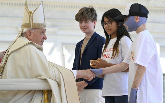 Pope Francis greets children bringing the offertory gifts during Mass in St. Peter's Square at the Vatican May 26, 2024, wrapping up the first World Children's Day held May 25-26. The pope shakes hands with Roman Oleksiv, a Ukrainian boy who lost his mother and suffered life-threatening burns from a Russian missile strike July 14, 2022. (CNS/Vatican Media)