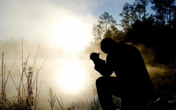 A man praying beside a lake (Unsplash/Aaron Burden)
