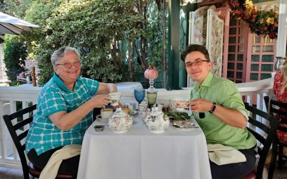 Two women sit at table drinking tea.