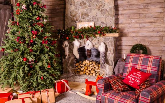 A Christmas tree with gifts underneath, near a fireplace with stockings