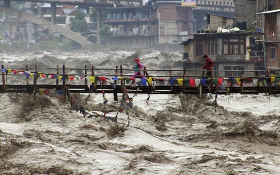 Residents run across a bridge over the flooding Beas River following incessant rains in Kullu, in northern Indian state of Himachal Pradesh, Aug. 26, 2025. (AP/Aqil Khan)