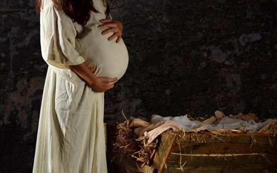 Pregnant Mary in a white robe stands next to the manger (Dreamstime/R. Gino Santa Maria)