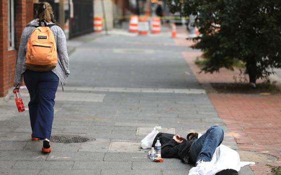 A woman walks past a homeless man sleeping on a sidewalk in Baltimore June 6, 2023. (OSV News/Bob Roller)
