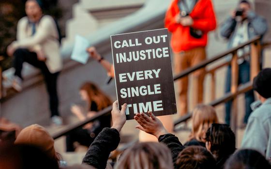 A sign reads, "Call out injustice every single time" (Unsplash/Colin Lloyd)
