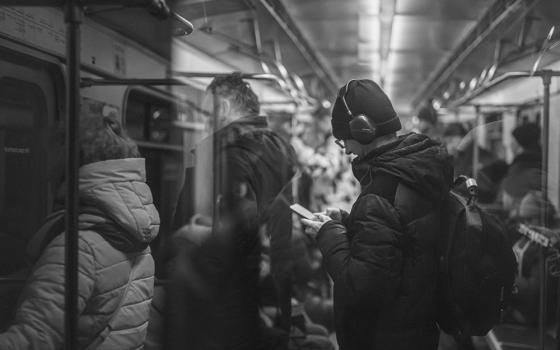People standing riding the subway, one wearing headphones and looking at a cellphone (Unsplash/Myznik Egor)