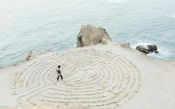 A person walks a labyrinth created by rocks near water's edge.