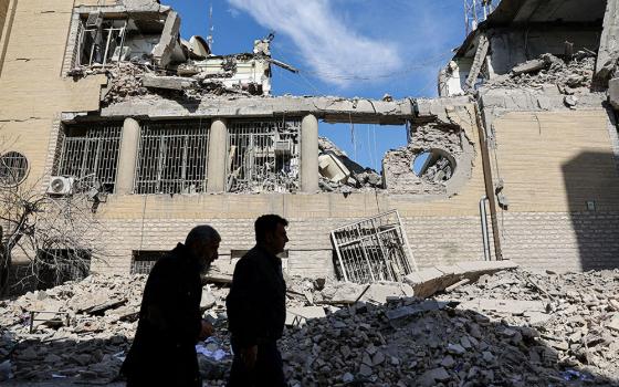 People walk past damaged buildings in Tehran, Iran, March 4, 2026, following a strike on a police station, amid the U.S. and Israel-Iran war. (OSV News/WANA via Reuters/Majid Asgaripour)