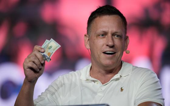 Peter Thiel, co-founder of PayPal and Palantir, offers a pair of hundred dollar bills to attendees during a keynote address at the Bitcoin Conference, April 7, 2022, in Miami Beach, Fla. (AP Photo/Rebecca Blackwell, File)
