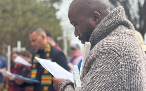Steven Nabieu Rogers, of the Africa Faith and Justice Network, prays while holding a cross outside the U.S. Department of Justice in Washington April 3, 2026, during the Way of the Cross on Good Friday. It feels as if the institutions of governance are not carrying out their role and as Catholics, there’s a need to pray about that, he said. (NCR photo/Rhina Guidos) 