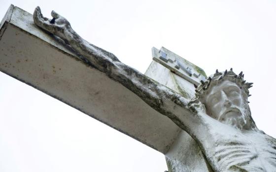 portion of a cement sculpture of crucifox shows Jesus' head and arm. 