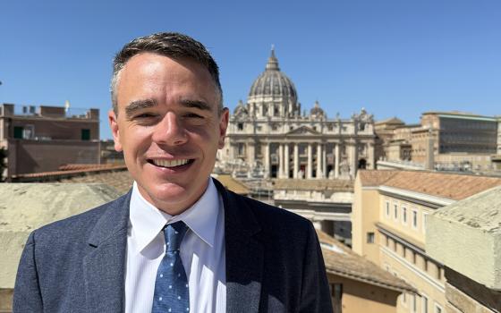 Michael J. O'Loughlin is pictured on the rooftop of the Jesuit Curia, with St. Peter's Basilica in the background, at the Vatican in September 2025. "Capturing the full range of experiences and individuals that make up the church is my goal as editor of NCR," writes O'Loughlin. (Courtesy of Michael J. O'Loughlin)