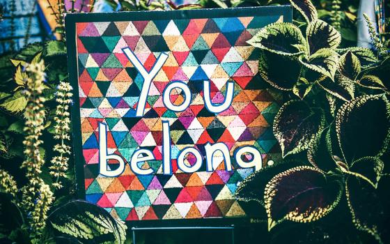 Colorful sign surrounded by plants says, "You belong" (Unsplash/Tim Mossholder)
