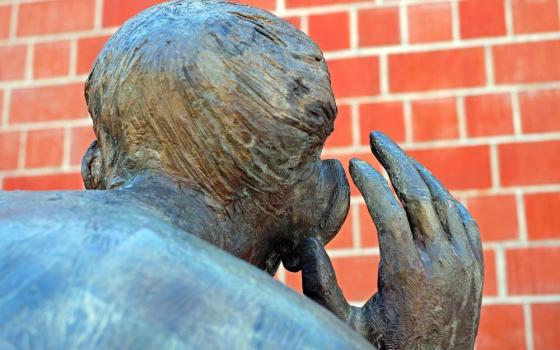Sculpture of back of a person's head, hand cupping ear.