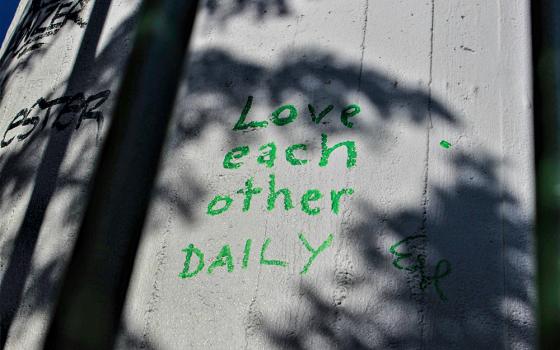 "Love each other daily," written on a fence with shadows of trees (Unsplash/Josefina Bartkova)