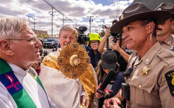 A member of the Illinois State Police, right, relays the message to clergy that U.S. Immigration and Customs Enforcement denied them access to detainees to provide Communion, outside an ICE facility in Broadview, Ill., Oct. 11, 2025. (AP/Adam Gray)