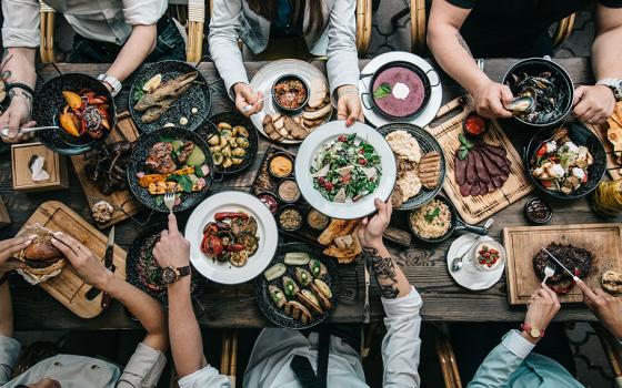 People eat and reach for food at a banquet table, viewed from above (Dreamstime/Olga Klochanko)