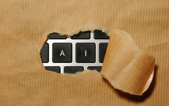 An illustration shows a package with wrapping torn away in the center, revealing a gray and black keyboard underneath. Through the tear the keys A and I are framed, spelling "AI."