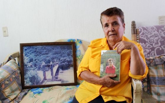 Guadalupe Lara in her home in Guadalajara, Mexico, with a copy of her memoir. A framed photograph of the historic Arcediano Bridge, which was destroyed during dam construction, rests at her side. (Tracy L. Barnett)