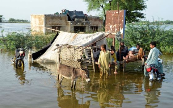 People wade in floodwaters outside their home, following heavy rains during the monsoon season in Sohbatpur district of Pakistan, Aug. 28. Experts say about one-third of the country is under water. (CNS/Reuters/Amer Hussain)