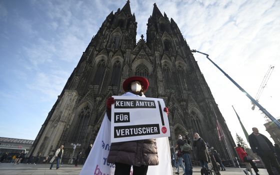 A participant of a rally of the initiative Maria 2.0 holds a poster with the inscription 'No offices for cover-ups' in front of the cathedral in Cologne, Germany, Thursday, Nov. 18, 2021. (Henning Kaiser/dpa via AP)