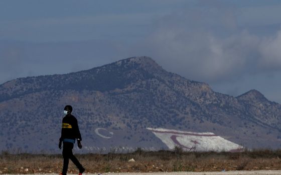 A migrant walks near Pournara migrant reception center in Kokkinotrimithia, as a giant Turkish Cypriot breakaway flag, right, and Turkish flags painted on a mountain are seen in the background in the Turkish occupied area of the ethnically divided island 