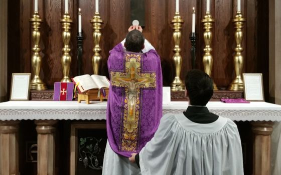 A priest elevates the Eucharist after consecrating it during a Latin Mass. (Creative Commons/Andrew Gardner)