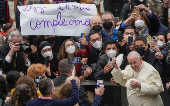 Pope Francis puts on a skull cap he was just presented with as he walks by a placard in Italian reading : "Today is my birthday", at the end of his weekly general audience in the Paul VI Hall at the Vatican, Wednesday, Feb. 02, 2022. (AP Photo/Gregorio Bo