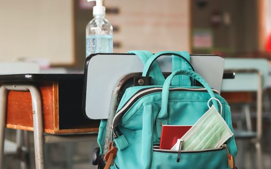 A disposable face mask is seen in a backpack hanging on a school desk holding a bottle of hand sanitizer. (Dreamstime/Phuttharak Chindarot)