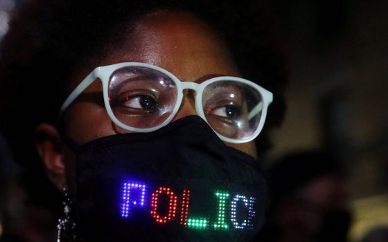 A person in a mask with lights spelling out at least the word "police" stands outside the site of the 2020 vice presidential debate between Vice President Mike Pence and Democratic vice presidential nominee Sen. Kamala Harris on the campus of the Universi