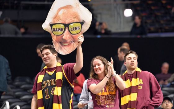 Three Loyola University Chicago students dressed in team colors, maroon and yellow, hold up a cardboard poster of Sr. Jean Dolores Schmidt's head